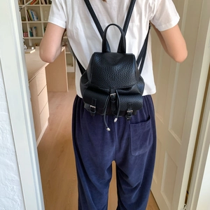 Detail view of black lychee texture leather backpack with flap drawstring and buckle pockets