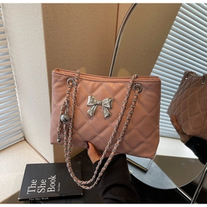 Detail view of pink quilted handbag with silver bow charm and chain strap being held
