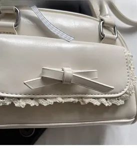 Close-up of bow decor and lace trim on a cream PU leather Boston crossbody handbag