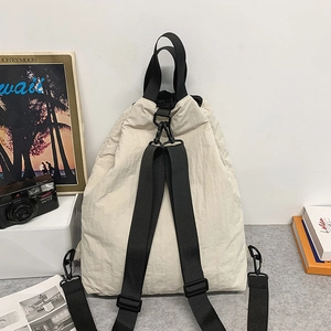 Detail eines beigen Nylon-Rucksacks mit Kordelzug, schwarzen Trägern und Metallschnallen