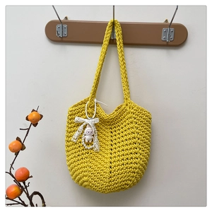 Detail of yellow chunky knit tote bag with white lace bow and plush charm on wood hanger
