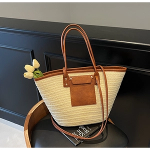 Detail of woven straw tote bag featuring brown leather trim and metal rivet accents
