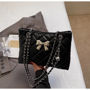 Detail of quilted leather bag featuring a silver metal bow and chain shoulder strap