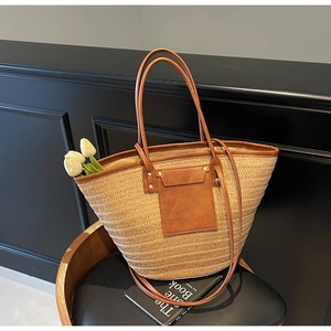 Detail of woven straw tote bag featuring brown faux leather handles and a front pocket