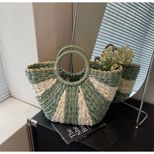 Detail of hand-woven straw tote with green and beige radial stripes and golden thread