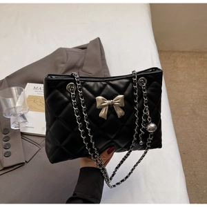 Close-up of black quilted shoulder bag with silver bow accent and metal chain strap