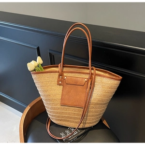 Detail of woven straw tote bag with brown leather handles on a modern chair with flowers