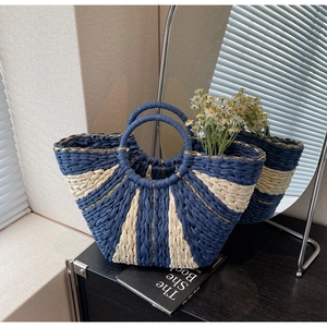 Detail of hand-woven straw tote featuring navy blue contrast and elegant gold silk stitching