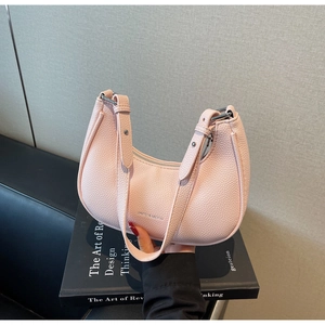 Close-up of pink pebbled leather half-moon bag with silver zipper on a black book