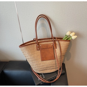 Detail of a straw woven tote bag featuring a leather front pocket and slim top handles