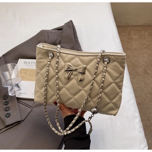 Detail of beige quilted bag featuring silver bow clasp and chain strap on a textured surface