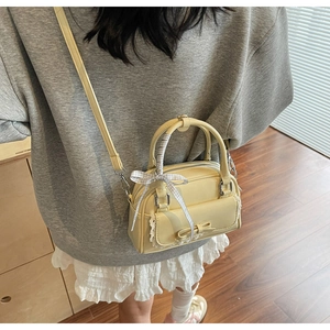 Detail of cream crossbody bag featuring a plaid bow, lace trim, and dual zippers