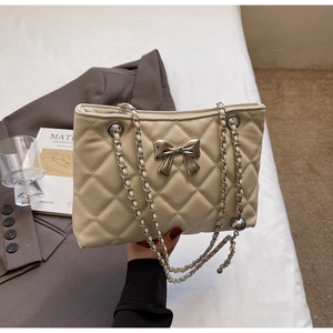 Detail of cream quilted leather bag featuring a silver bow buckle and chain strap