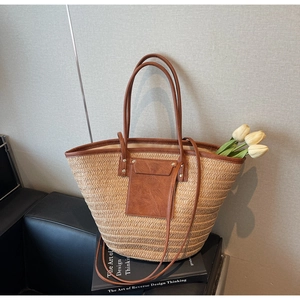 Detail of a woven straw tote bag with brown faux leather handles and tulip decorations
