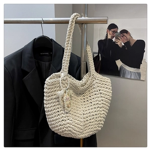 Detail of cream woven shoulder bag with pearl chain and character pendant on a rack