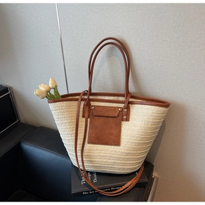 Detail of woven straw tote bag with brown leather pocket and metallic rivet accents