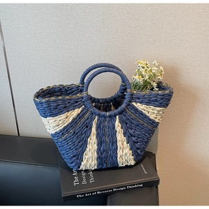 Detail of contrast woven straw bag with circular handles and golden thread accents