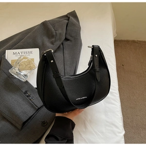 Detail of black crescent shoulder bag with lychee texture and silver logo on bed