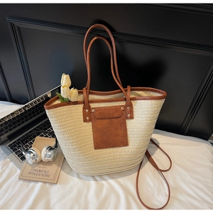 Detail of woven straw tote bag with brown leather trim and shoulder straps on white cushion