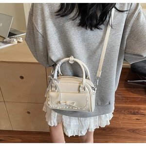 Detail of cream Boston bag with bow pocket and plaid scarf handle shown on model