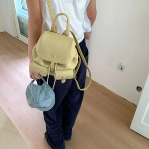 Rear view of a model wearing a light yellow pebbled leather backpack with metal buckles