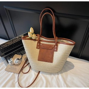 Detail of a woven straw tote bag with brown leather trim, rivets and a front pocket