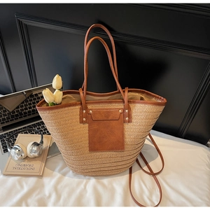 Close-up of woven straw tote bag with brown faux leather pocket and metal rivet details