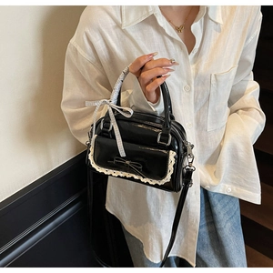 Detail of black patent leather crossbody bag with lace trim and silk scarf handle decor