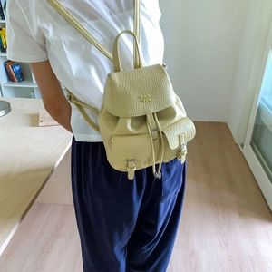 Detail of a creamy yellow lychee texture leather backpack with drawstring and flap pockets