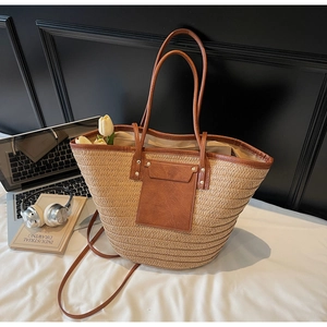 Detail of woven straw tote bag with brown leather trim and metallic rivet accents