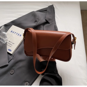 Détail d'un sac à bandoulière rectangulaire marron foncé sur un fond urbain épuré