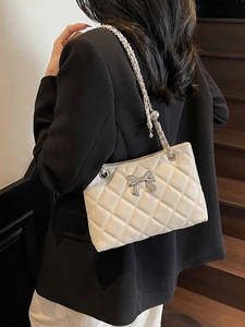 Quilted beige shoulder bag with silver bow accent and adjustable chain strap worn by model