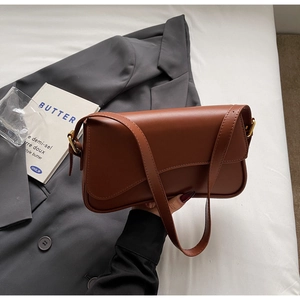 Gros plan sur le sac sous le bras en cuir marron avec boucle dorée sur un blazer gris
