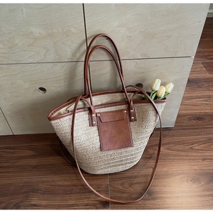 Detail of woven straw tote bag featuring brown leather straps and metal rivets
