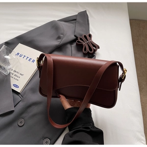 Détail d'un sac baguette en cuir mat marron foncé avec une boucle en métal doré