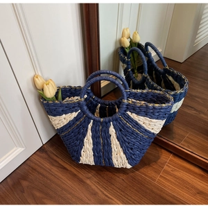 Detail of navy and beige woven straw tote with round handles and gold trim accents
