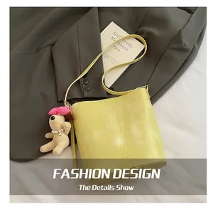 Detail der hellgelben Beuteltasche mit Plüschanhänger auf modischem Anzug-Hintergrund