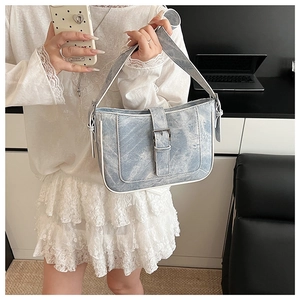 Detail of light blue denim crescent bag with white piping and silver buckle closure