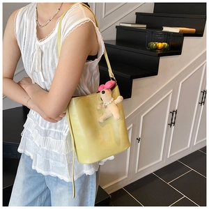 Detail of light yellow leather bucket bag with SNML logo and plush dog charm on a model