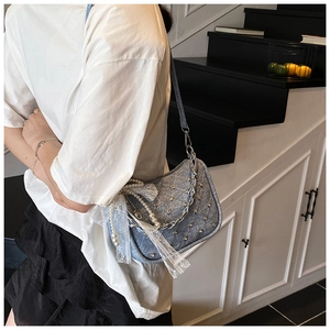 Détail du sac matelassé en jean bleu avec rivets argentés et chaîne en perles avec nœud