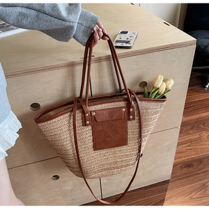 Detail of woven straw tote bag with brown leather handles and a decorative front pocket