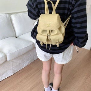Detail of a light yellow pebbled leather mini backpack with buckle pockets in a home setting