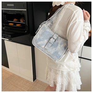 Detailed side view of a light blue denim crescent bag with white piping and silver buckle
