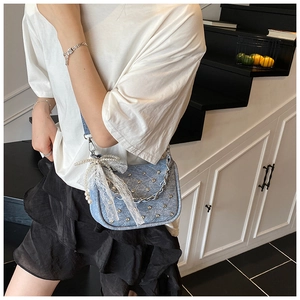 Détail du sac en jean bleu clair avec clous argentés et nœud en dentelle et perles
