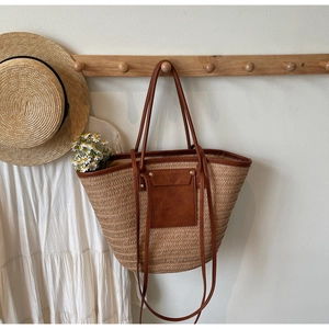 Detailed straw tote bag with brown leather straps hanging in a beach scene