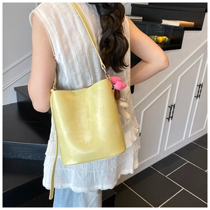 Detail of yellow bucket bag with plush charm and SNML logo on minimalist white dress
