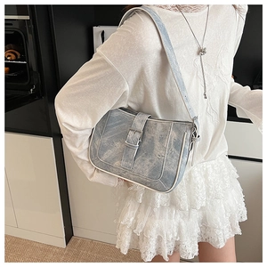 Detail of light blue washed texture crescent bag with silver buckle and white trim decor