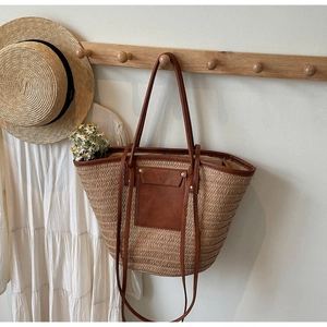 Close-up of a woven straw tote bag with brown leather handles on a wooden hook