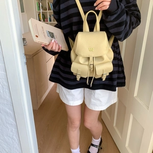 Detail of a beige lychee leather mini backpack featuring a drawstring and buckle closure