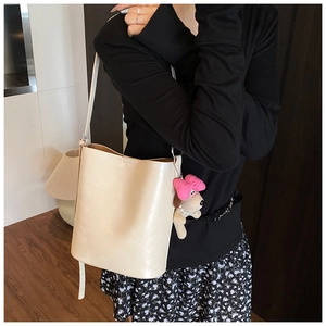 Detail of off-white bucket bag with SNML embossed logo and cute pink plush charm